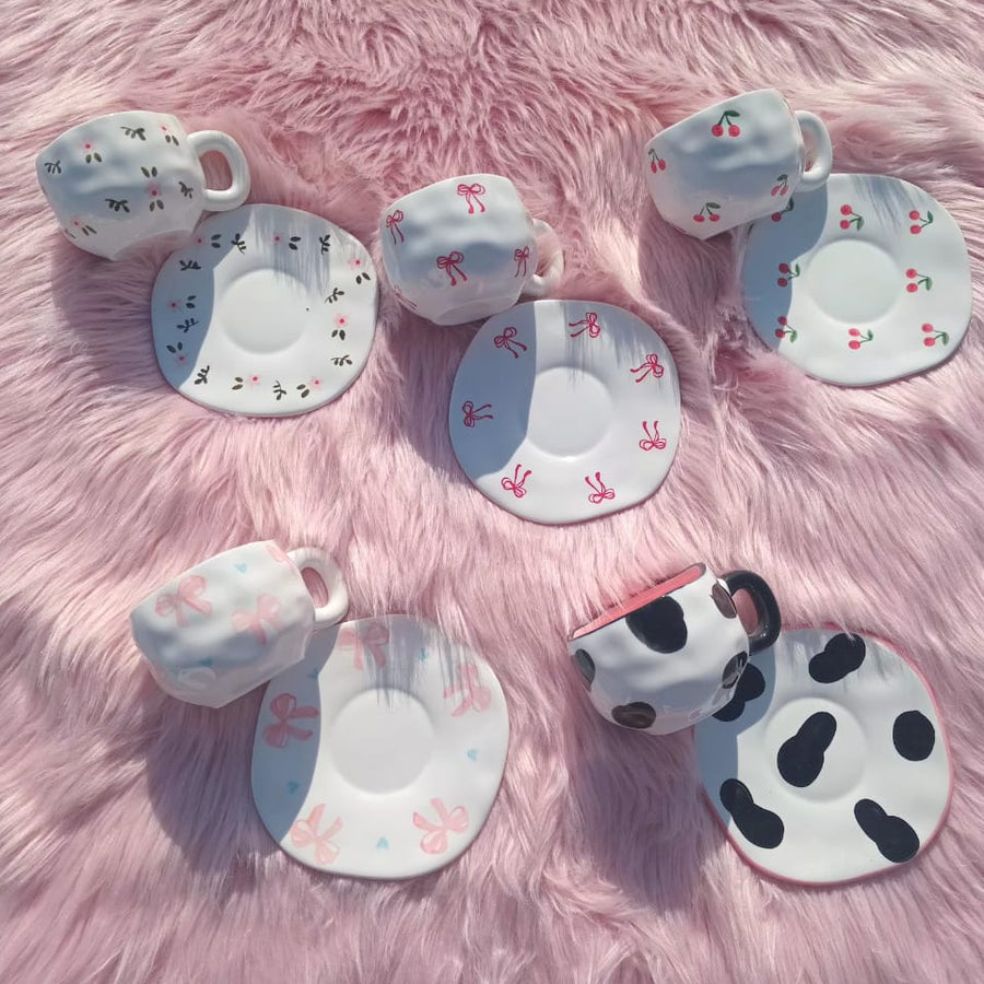 Set of ceramic teacups and saucers with various designs on a pink fluffy surface