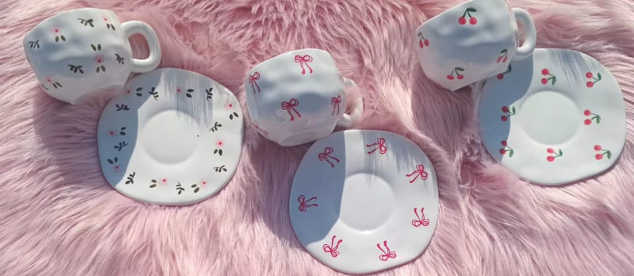 Set of ceramic teacups and saucers with various designs on a pink fluffy surface